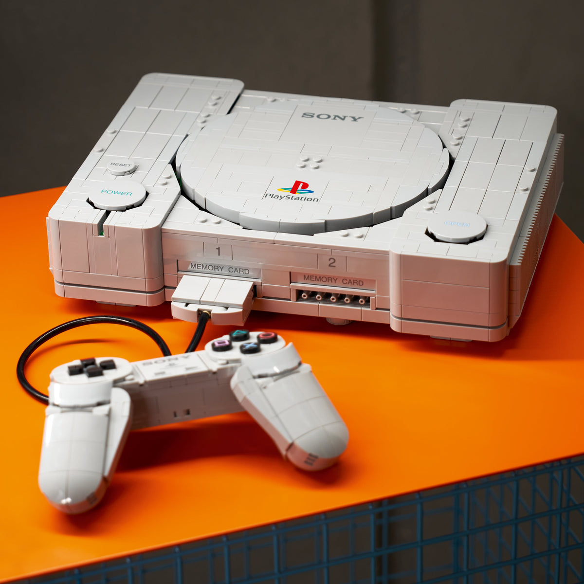 Console PlayStation™ en briques LEGO avec manette, posées sur une table orange